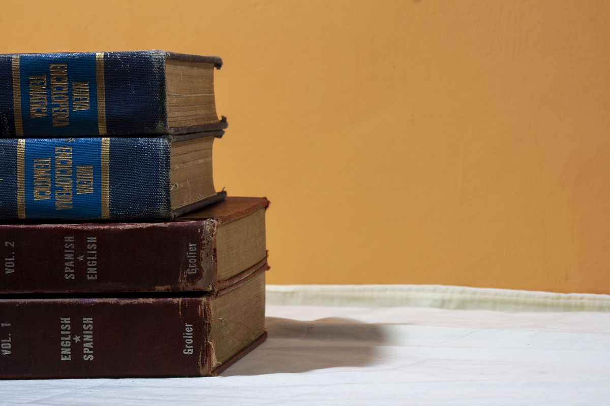 A close-up of vintage English-Spanish dictionaries stacked on a table against a warm backdrop.